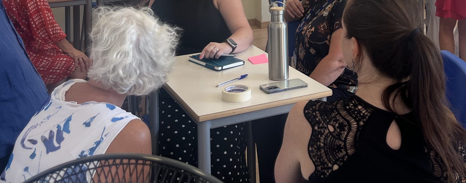 Teachers at Andersen International School, Milan, gathered around a table with notebooks on Day 1, seen from behind